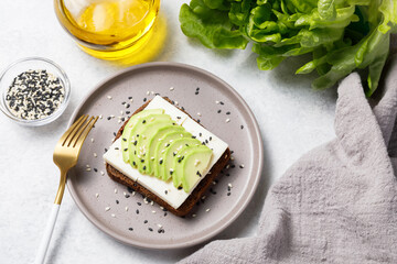 Rye bread toast with goat cheese and avocado on white stone table background. Flat lay, top view