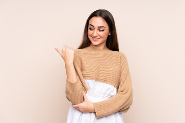 Young caucasian woman isolated on beige background pointing to the side to present a product