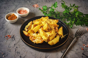 Delicious lunch: baked potatoes with cheese on a black plate on a gray background