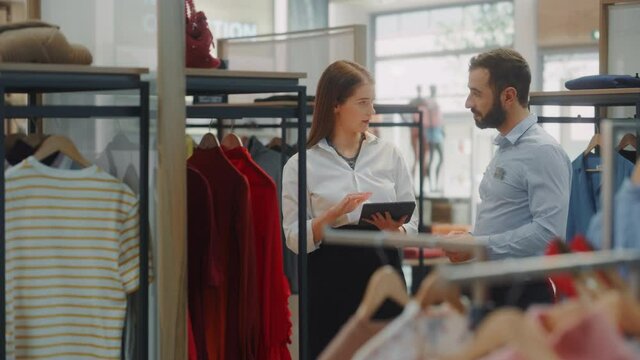 Clothing Store: Businesswoman Uses Tablet Computer, Talks to Visual Merchandising Specialist, Collaborate To Create Stylish Collection. Business Owner's Fashion Shop: Sales Manager Talks to Designer