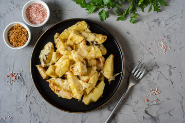 A hearty snack: potato slices baked with spices and cheese. Potatoes and cheese on a beautiful plate on a gray background. Top view