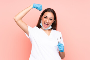 Woman dentist holding tools isolated on pink background celebrating a victory