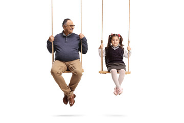 Mature man sitting on a swing and looking at a little girl