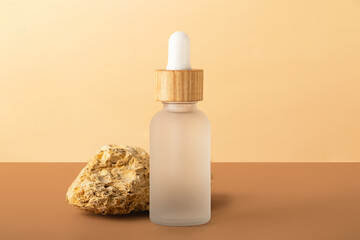 Cosmetics bottle with dropper from frosted glass.Decorative beige stone behind.Pastel isometric background.Concept of the organic,zero waste mock up packaging.