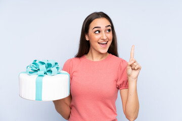 Pastry chef holding a big cake isolated on blue background intending to realizes the solution while lifting a finger up