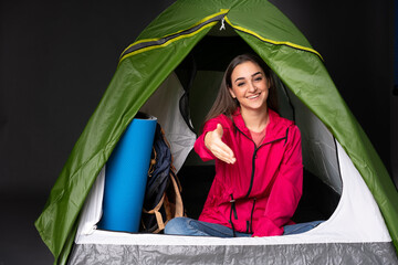 Young caucasian woman inside a camping green tent shaking hands for closing a good deal