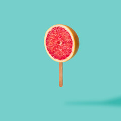 Ice cream on stick made with red grapefruit on mint blue background. Summer fruit creative concept.