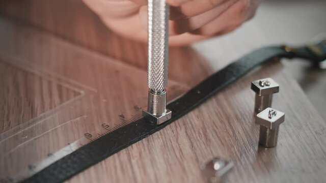 Close up of hands of leather worker in an attempt to stam letter on leather bracelet. Accessories.