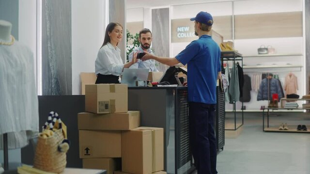 Clothing Store Checkout Cashier Counter: Retail Sales Managers Pack and Give Package Delivery Courier to Deliver Online Order. Fashion Shop Designer Brands Made Available with Online Shopping