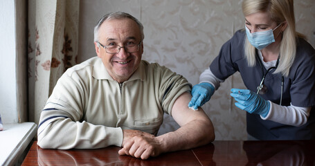 Obraz premium Young woman doctor injecting vaccine to elderly man during home visit