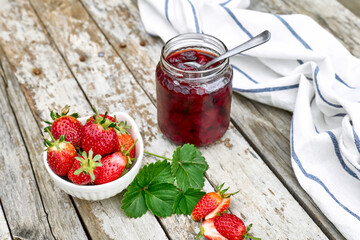 Strawberry jam in a jar and fresh red ripe organic bio strawberries in a bowl on wooden table in the garden. Spring or summer harvesting. Healthy eating. Vitamin.