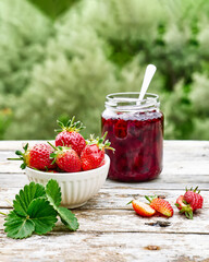 Strawberry jam in a jar and fresh red ripe organic bio strawberries in a bowl on wooden table in the garden. Spring or summer harvesting. Healthy eating. Vitamin. - obrazy, fototapety, plakaty