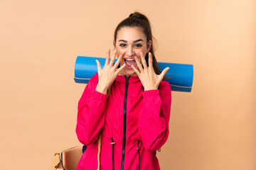 Young mountaineer girl with a big backpacker isolated on beige background with surprise facial expression