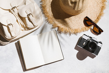 Summer holiday concept. Travel flat lay with notepad, camera, backpack, and hat on white table background. Top view, mockup