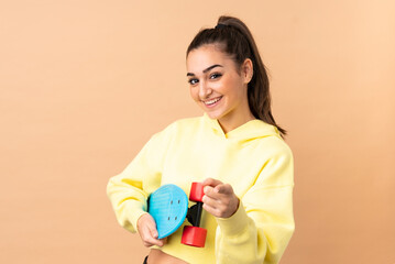 Young caucasian woman isolated on pink background with a skate and pointing to the front