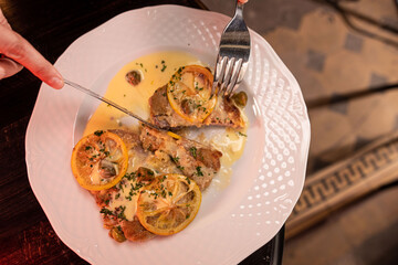 Woman hands cutting veal piccata served in a sauce using a fork and knife close-up, shallow focus