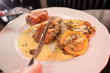 Woman hands cutting veal piccata served in a sauce using a fork and knife close-up, shallow focus