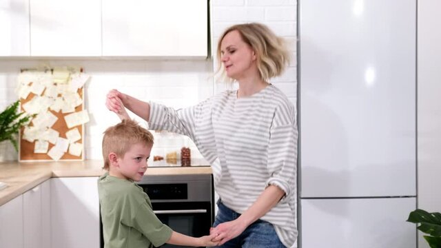 Excited mom or babysiter and kid boy jumping, dancing, laughing in modern scandinavian house kitchen. Happy family mother and son having fun enjoy playing singing together at home
