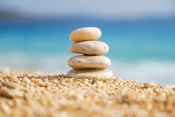 Fototapeta na wymiar Pyramid stones balance on the sand of the beach. The object is in focus, the background is blurred. Zen balance, minimalism, harmony and peace