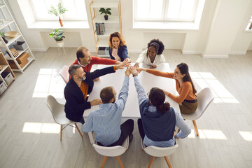 Diverse team of happy enthusiastic people join hands. Multiethnic teammates, business partners and friends motivating each other in group meeting around office table. Teamwork, participation concept
