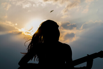 Silueta de mujer tocando la guitarra con el sol detras