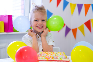 Fototapeta na wymiar Excited Birthday boy with colorful balloons near birthday rainbow cake. Festivel background. Funny birthday party.