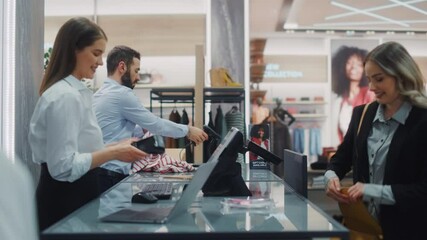 Clothing Store Checkout Cashier Counter: Beautiful Young Woman Buys Clothes from Friendly Retail Sales assistant, Paying with Contactless Credit Card. Fashion Shop with of Designer Brands. Medium Shot