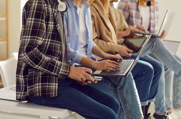 Middle section of young people in casual clothes using gadgets sitting together on table. University or college student using different digital device as mobile phone, laptop, tablet for study
