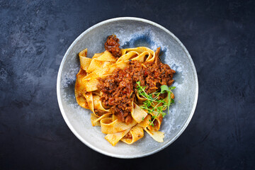 Modern style traditional Italian ragu alla bolognese sauce with papedelle pasta noodles and parmesan cheese served as top view in a ceramic design bowl with copy space - obrazy, fototapety, plakaty