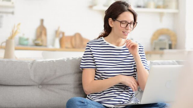 Happy millennial woman with laptop hold hands in pray sit on sofa look with hope on computer monitor. Casual worry female in eyewear check email, results of interview for remote work, lottery winners
