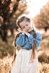 Smiling blonde kid girl 4-5 year old wearing casual trendy clothes resting over sunny natural background with cloed eyes. Childhood. Spring seson. Happiness.