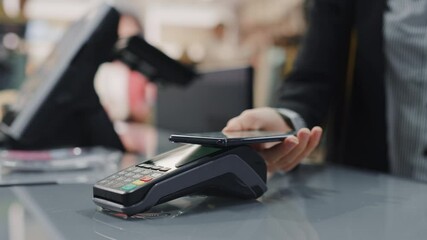 Clothing Store: Woman At Counter Buys Clothes Paying with Smartphone Through, Contactless NFC Terminal. Department Store, Shopping Center, Mall Purchase. Close-up Focus on Mobile Phone - Powered by Adobe
