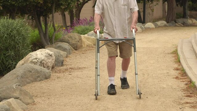 Happy, smiling senior man (82 year old Caucasian) walking in the park using a walker