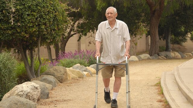 Happy, smiling senior man (82 year old Caucasian) walking in the park using a walker