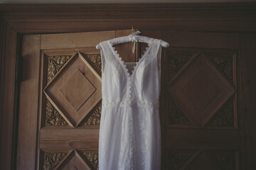 A cream vintage wedding dress hangs from a wooden door