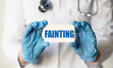 A medical worker in gloves holds a card with the words FAINTING. Medical concept.