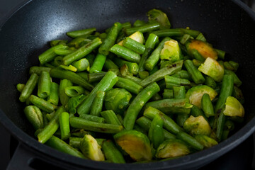 Fried green beans and brussels sprouts in frying pan close-up. Easy vegan recipe of vegetarian food. Healthy food concept. Selective focus.