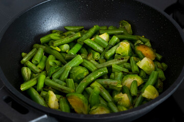 Stewed brussels sprouts and green beans in pan close-up. Easy recipe of vegan and vegetarian food full of vitamins and clean eating. Healthy food concept. Selective focus.