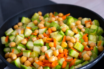 Hot vegan salad. Stewed vegetables with chickpeas, zucchini and carrot in frying pan. Healthy nutrition, vitamins, diet, clean eating, vegan and vegetarian food. Healthy food concept. Selective focus.
