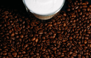 Brown coffee beans as background, with a cup of cappuccino. View from above