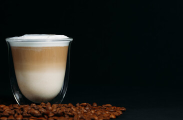 Close-up of a special glass transparent thermo cup with cappuccino. Beautiful layers of milk and coffee. Scattered coffee beans. Copy space