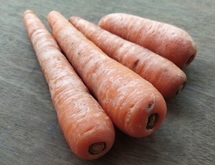 Isolated bunch of organic farm fresh carrots stacked together from small to big without washing after harvesting on wooden table background. Horizontal Closeup top view.