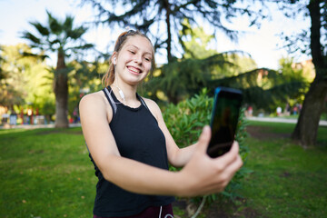  a beautiful green-eyed red-haired girl in a medium shot smiles while taking a selfie with her phone and listening to music
