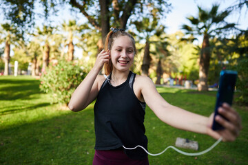 a beautiful red-haired girl with green eyes in a medium shot stretches her muscles to be able to start playing a sport in a park in the center of the city