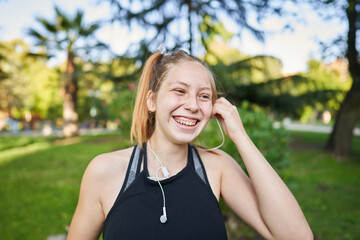 a beautiful red-haired girl with green eyes puts on your headphones to listen to her favorite music before exercising in a park near the city