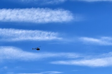 Fototapeta na wymiar small silhouette of helicopter against big white cloud on blue sky