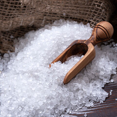 White sea salt for cooking food on a dark wooden table, natural spoon and coarse bag