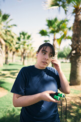 Fototapeta premium beautiful white woman with brown hair and a sports outfit puts on her headphones to start playing sports in a park near the city center