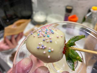 Red layered sweet strawberry tempered in white melted Belgian beautiful chocolate with decorations on a stick. Making chocolate covered strawberries