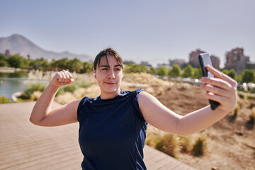 A beautiful white woman with brown hair and a sports suit takes a selfie exercising and listening to music in a park in the city center